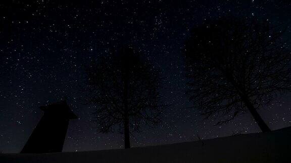 星星在夜空中移动木制的钟楼和树木的剪影在冬天天文时间流逝摄影