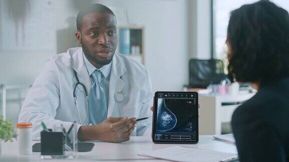 非裔美国医生在健康诊所用平板电脑向病人展示乳房x光检查结果友善助理讲解预防乳腺癌筛检的重要性