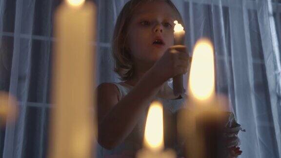 一个白人女孩拿着洋娃娃吹灭蜡烛的肖像一个奇怪的孩子晚上站在大窗户前的烛光下恐慌、恐惧、陌生