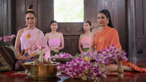 一群穿着泰国传统服装带着鲜花的泰国妇女呆在古老的房子里向照相机表示敬意
