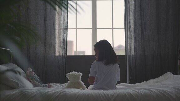 坐在病床上的小女孩抱着娃娃看向窗外