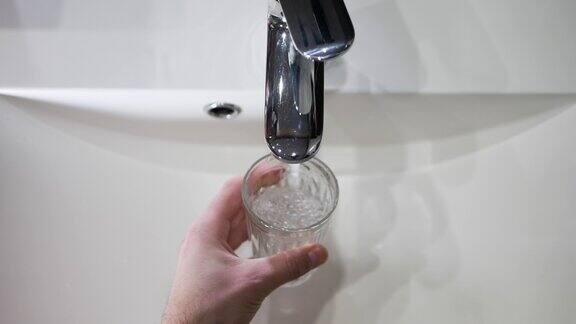 一个男人的手拿一个杯子到水龙头前把水从水龙头里倒进一个透明的杯子里