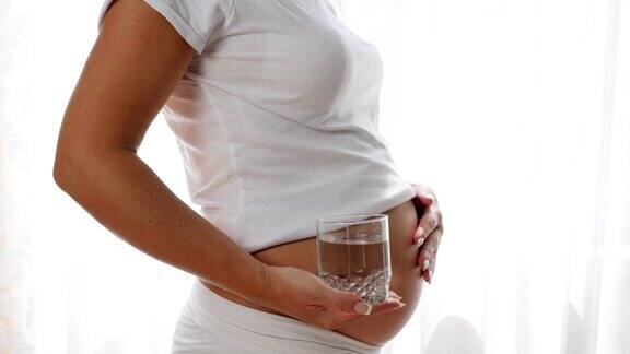 肚子大的孕妇保持玻璃矿泉水抚摸裸露的肚子