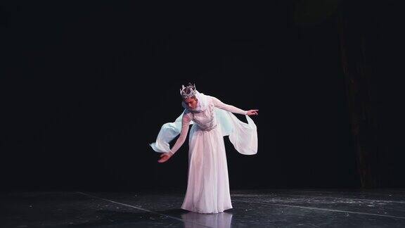 一位优雅、勤劳的芭蕾舞女演员头戴皇冠在黑色背景上摆出美丽的姿势风吹着她美丽的白色套装