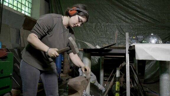 女铁匠戴着保护耳机在她的diy车间里用锤子敲打金属棒来把它弄直