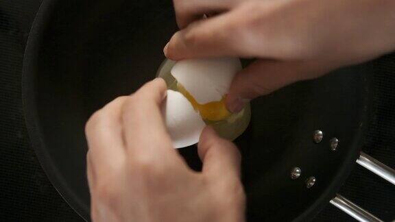 用手在黑色平底锅上敲鸡蛋的慢动作镜头
