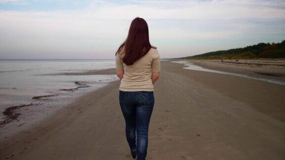真实的女人沿着海滩散步从后面看