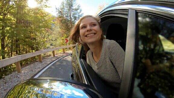 这是一个快乐的年轻女子在秋天的公路旅行中从车窗探出头来的照片