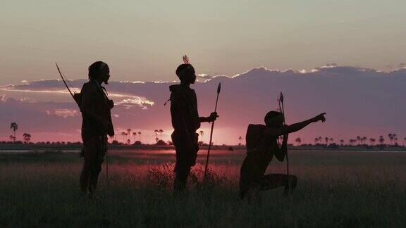 在博茨瓦纳的Makgadikgadi草原上夕阳下三名桑族人丛林人穿着传统服饰寻找动物的4K壮观的侧面画面