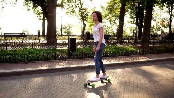 穿着蓝色牛仔裤和白色运动鞋的年轻女子在日出的公园玩滑板滑板的腿Slowmotion拍摄