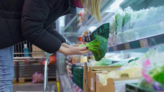 为了防止新冠肺炎疫情戴着医用口罩的妇女在超市选择蔬菜购买新鲜蔬菜花椰菜