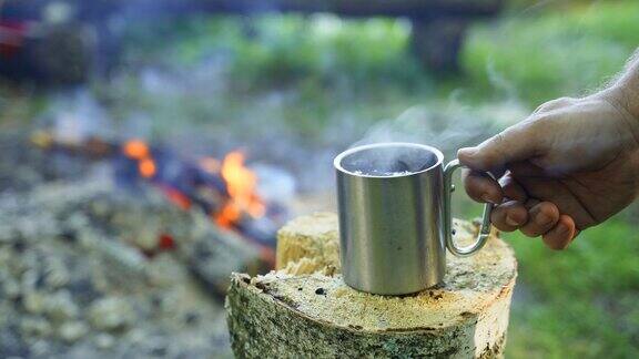 一个男人从火炉旁的树桩上拿了一杯热凉茶