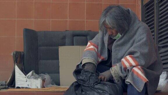 4K戴着医用口罩的无家可归老人坐在城市的人行道上
