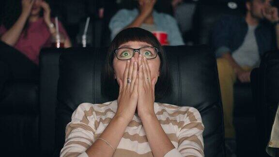 3.受了惊吓的女孩戴着眼镜捂着眼睛在电影院里看恐怖电影