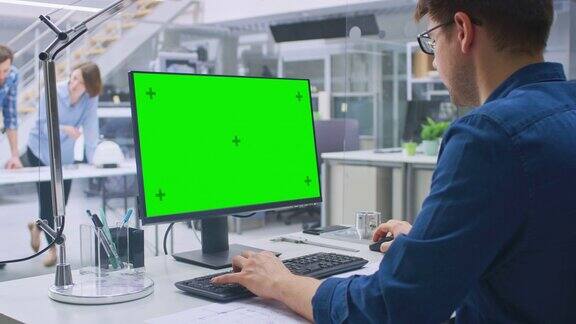 OvertheShoulderShot的工程师工作与绿色模拟屏幕桌面计算机在背景工程设施与工业设计的蓝图和图纸专家一起工作