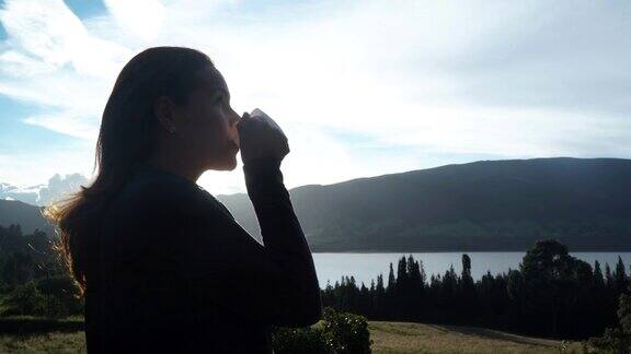 拉丁女人手里拿着一杯咖啡欣赏森林里的日落