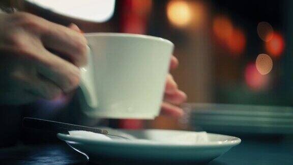 一位老妇人正轻轻地拿起一杯咖啡喝着然后拿回一个盘子在咖啡馆里特写视图