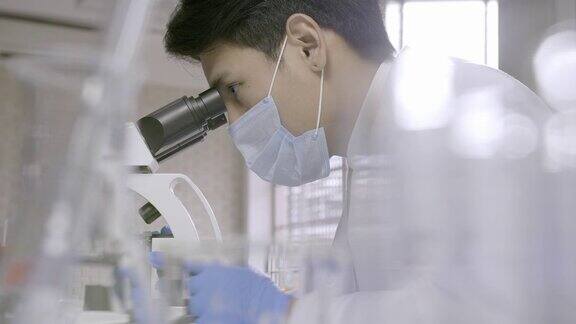 在实验室里通过显微镜进行研究的亚洲科学家