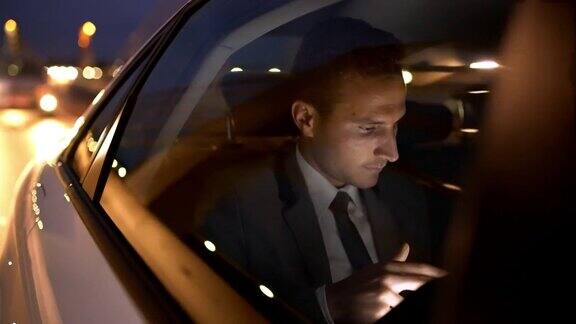 微软商人在一辆豪华轿车里使用平板电脑在夜晚的城市里