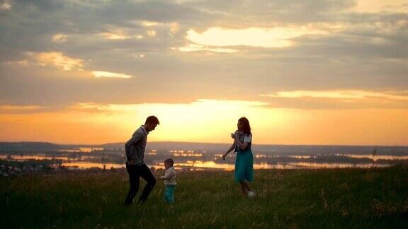 年轻的父母和他们的小儿子快乐地玩耍母亲和婴儿跑来跑去明亮的夕阳夏夜