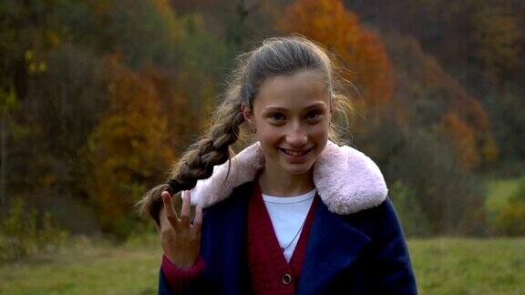 一个美丽的年轻女孩站在秋天的森林里看着相机微笑着她是快乐的缓慢的运动