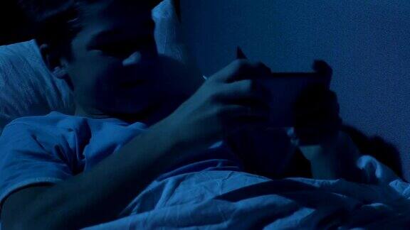 兴奋的青少年晚上躺在床上玩手机游戏自律