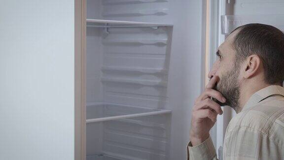 一个男人看着一个空冰箱