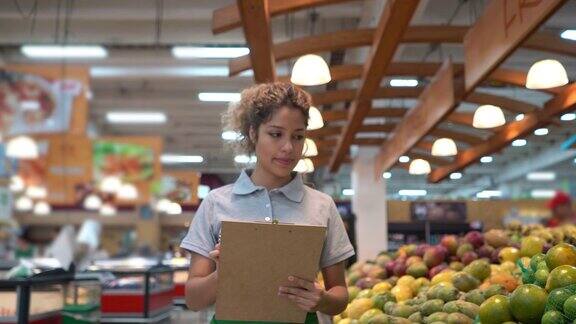 拉丁美洲美丽的女售货员检查水果零售展示和库存在剪贴板上