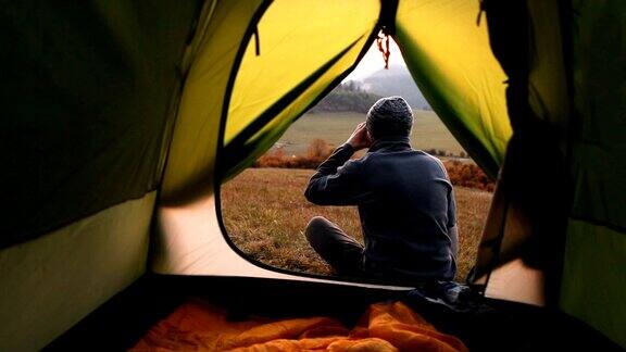 一个人端着一杯热茶坐在露营帐篷附近