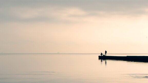 清晨两名男子站在防波堤上钓鱼