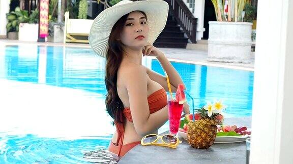 夏天性感的亚洲女人在橙色比基尼与热带饮料在游泳池