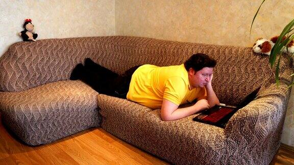 一个胖子躺在客厅的沙发上用笔记本电脑年轻人上网上网看新闻