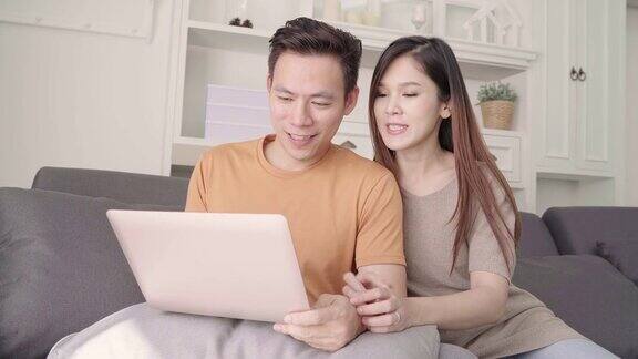 亚洲情侣在家里的客厅里用笔记本电脑搜索网络甜蜜的情侣在家里放松的时候躺在沙发上享受爱情的时刻生活方式夫妇在家里放松