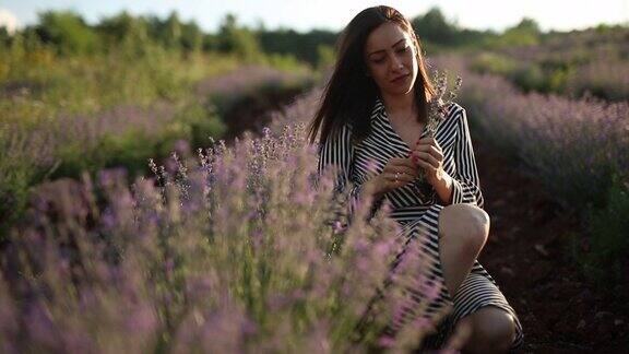 年轻女子蹲在薰衣草地里闻着一束薰衣草
