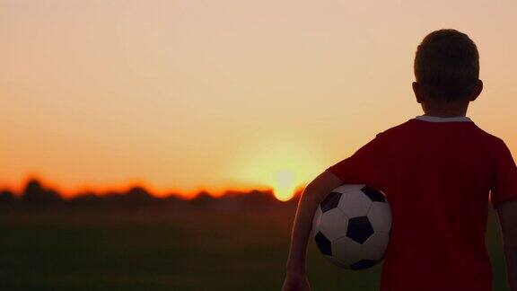 年轻的足球运动员带着球在球场上梦想着自己的足球生涯夕阳西下望着太阳
