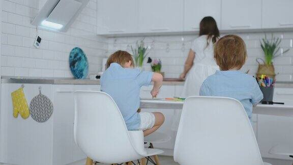 妈妈在厨房里洗盘子儿子坐在桌前用纸上画画