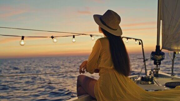 黄昏时身着黄色连衣裙的年轻女子欣赏着风帆