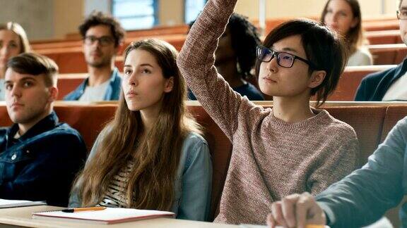 在课堂上聪明的亚洲学生举手向讲师提问多元种族的现代聪明学生在学院