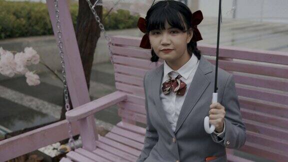 日本女学生穿着校服坐在吊椅上拿着透明的雨伞