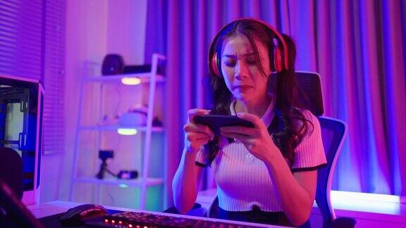 亚洲美女电竞女玩家在智能手机上玩手机游戏迷人的年轻女孩游戏玩家享受技术直播同时在家里的霓虹灯房间玩网络比赛