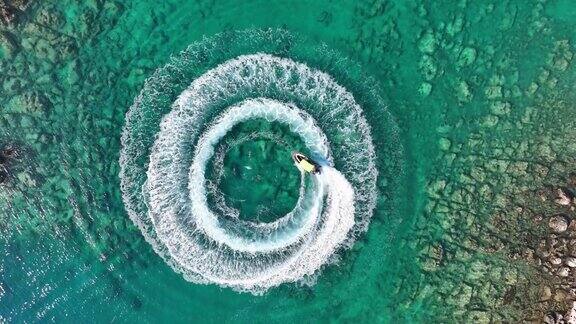 4K缩小令人惊叹的鸟瞰图的人驾驶个人船只在海洋中创建一个直下的圆形图案惊人的夏季背景水彩和美丽明亮清澈的绿松石热带海滩冒险的一天旋转的速度船
