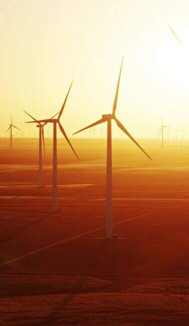无人机飞行过去的风力涡轮机在堪萨斯州农田与戏剧性的阳光-垂直