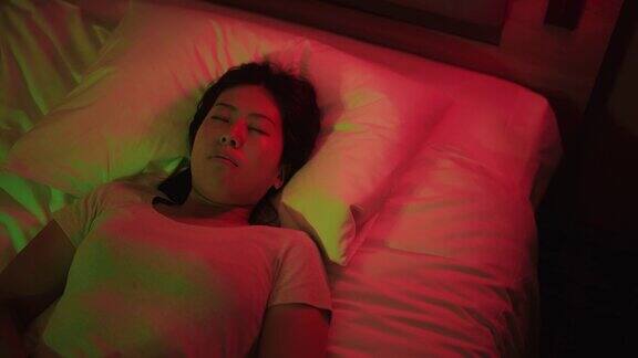 年轻女子被红色和绿色的霓虹灯照亮躺在家里卧室的床上休息