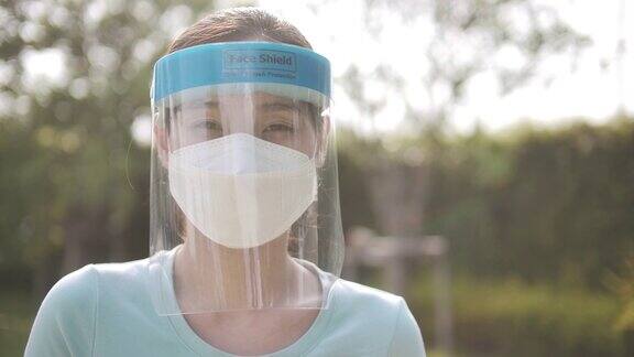 亚洲妇女的肖像戴外科口罩和面罩的冠状病毒预防户外看着相机