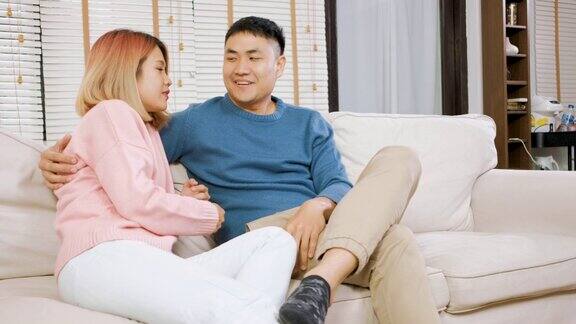 一对亚洲夫妇坐在沙发上拥抱大笑情侣在家里