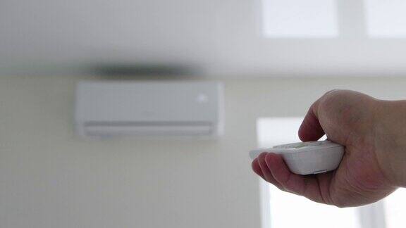 该男子手里拿着空调遥控器控制着公寓内舒适的空气温度现代分体式空调系统