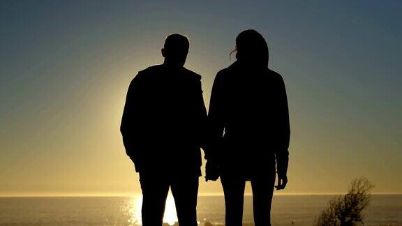 一对夫妇在日落时手牵手在海滩上散步的剪影