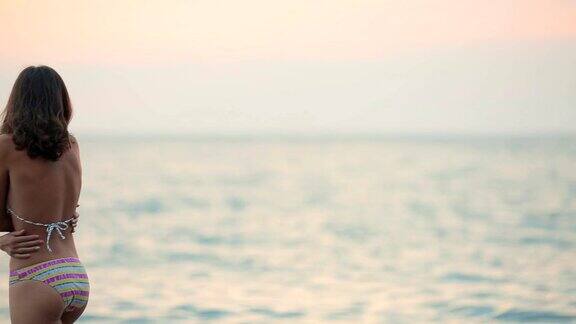 苗条的女人穿着比基尼在美丽的日落海边