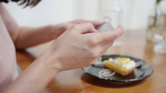 近距离亚洲妇女的手使用智能手机拍照的柠檬蛋糕在一家餐厅