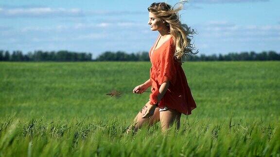 一个美丽的金发年轻快乐的女人的全长肖像在红色的衬衫慢慢地走在绿色的田野